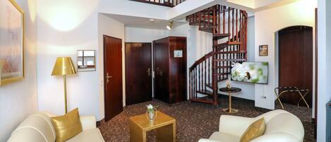 A spacious living area with a high ceiling, a staircase, and a flat-screen TV mounted on the wall.