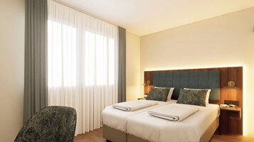 Habitación de hotel con cama, una silla, mesita de noche y ventana con cortinas.