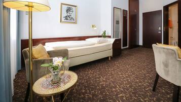 A hotel room with a bed, a sofa, a small table with a vase of flowers, a lamp, and a framed picture on the wall.
