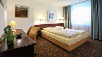 Quarto de hotel com cama, abajures, escrivaninha com luminária, espelho e janela com cortinas.