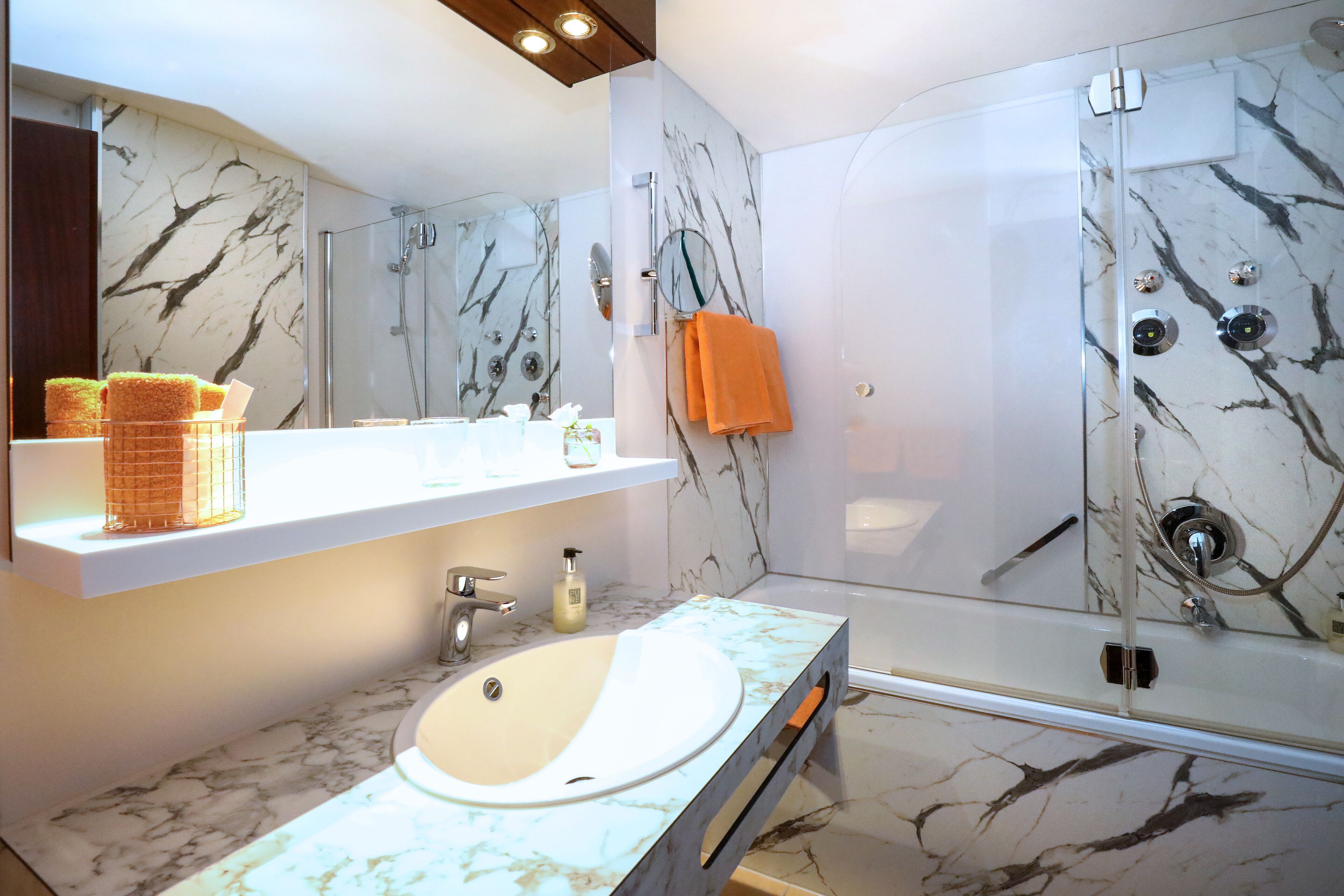 A modern bathroom with a marble sink, a glass-enclosed shower, and a mirror above the sink.