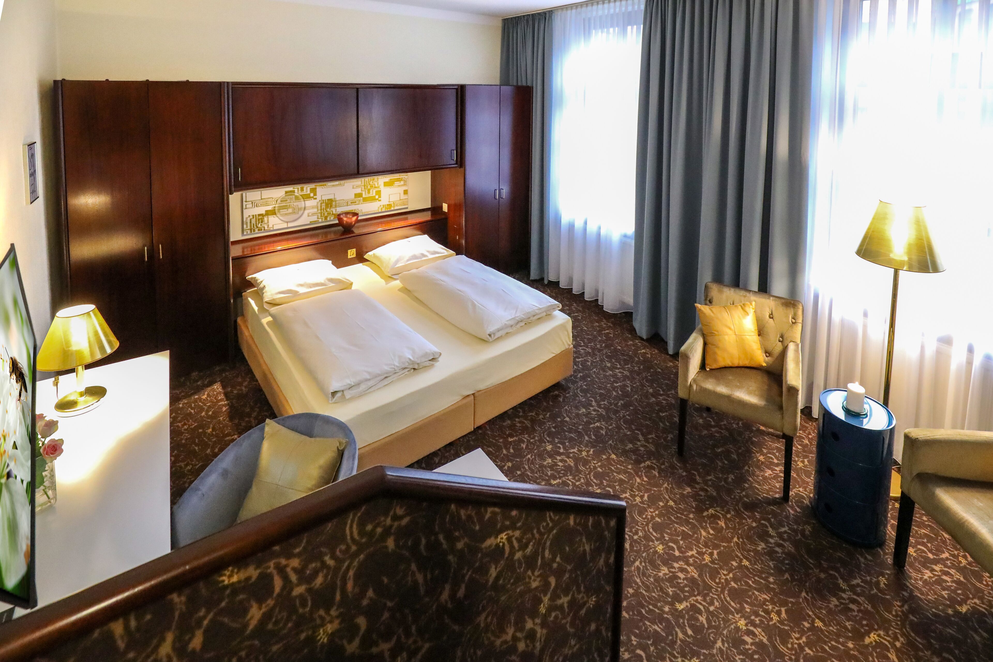 A hotel room with a large bed, a desk with a lamp, a chair, and a small table.