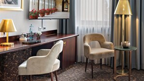 A hotel lobby with a reception desk, two armchairs, a standing lamp, and a television displaying a corridor with potted plants. - City-Hotel Aschaffenburg (Aschaffenburg)