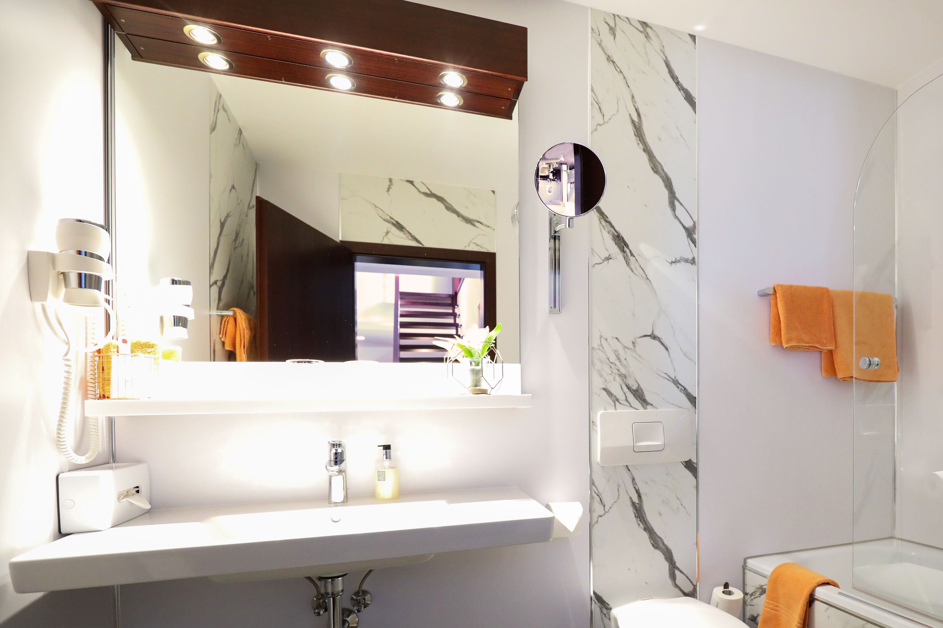 A modern bathroom with a large mirror, white sink, and marble walls.