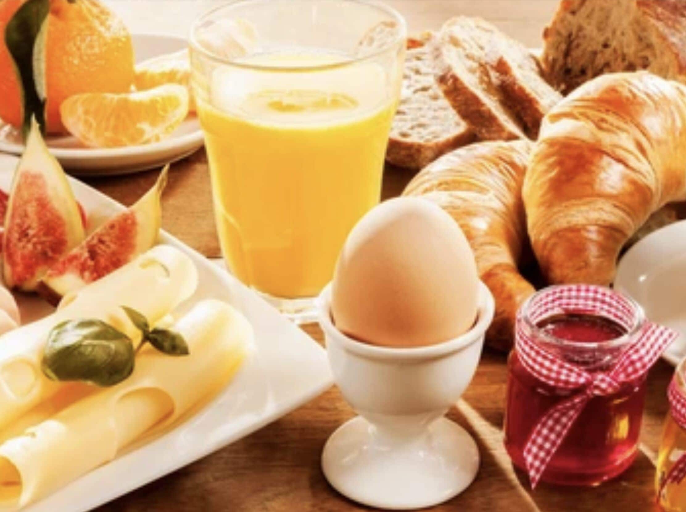 A breakfast setting with croissants, orange juice, eggs, and jam.