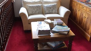 A living room with a sofa, a coffee table with books, a wooden cabinet, and a red carpet. - Claddagh Guest House (Oxford)