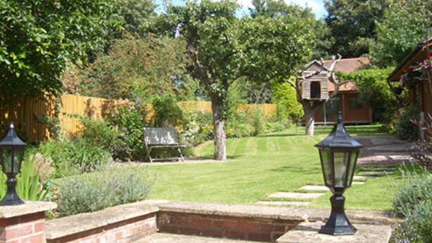 A well-maintained garden with a lawn, a wooden house, and a brick wall. - Claddagh Guest House (Oxford)