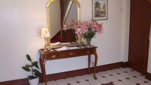 A wooden console table with a mirror, a vase of pink flowers, a lamp, and a framed picture on the wall. - Claddagh Guest House (Oxford)