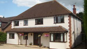A two-story house with a brown roof, white walls, and a brick extension on the right. There are flower baskets on the porch and a chimney on the roof. - Claddagh Guest House (Oxford)