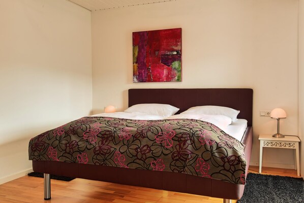 A bed with a floral-patterned bedspread, a dark headboard, and a wall-mounted abstract painting. - Weingut & Gästehaus Christoph Clüsserath (Trittenheim)