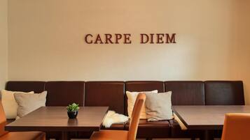 A dining area with a long wooden table, brown leather booth seating, and a wall-mounted sign that reads "CARPE DIEM".