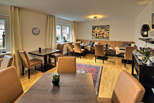 A modern dining area with multiple tables and chairs, a clock on the wall, and a colorful abstract painting. - Weingut & Gästehaus Christoph Clüsserath (Trittenheim)