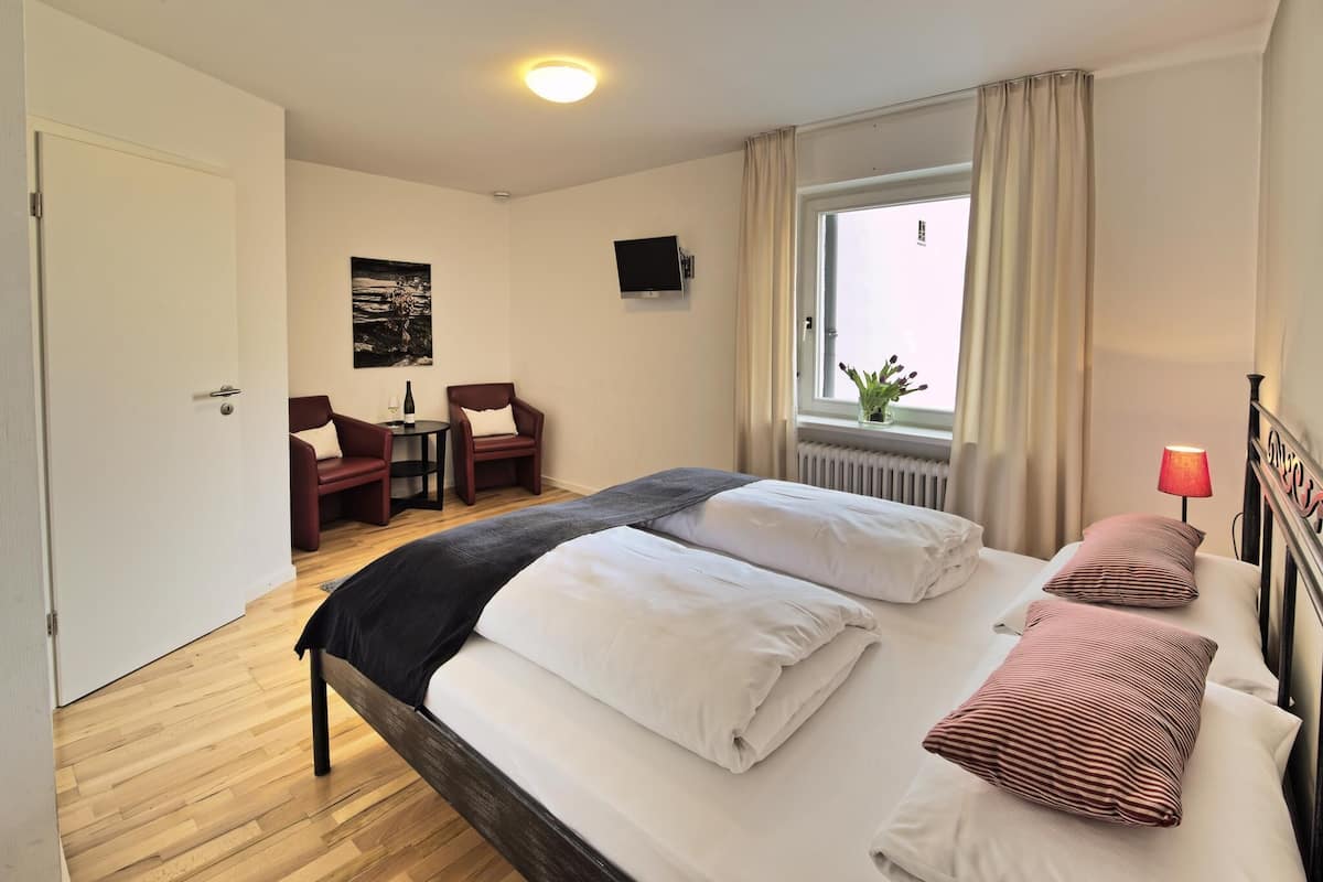 A hotel room with a bed, a desk with a chair, a TV, and a window with curtains.