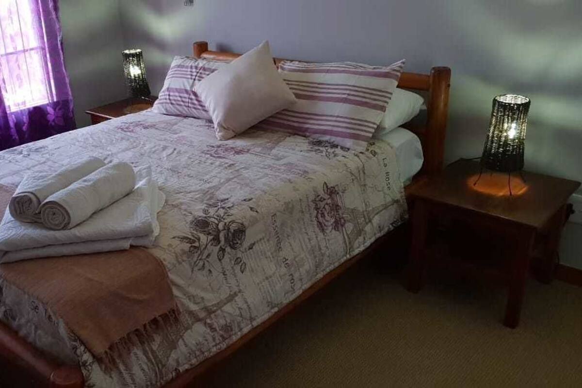 Una cama bien tendida con toallas enrolladas, una colcha de estampado floral y dos lámparas de noche sobre mesitas de madera.