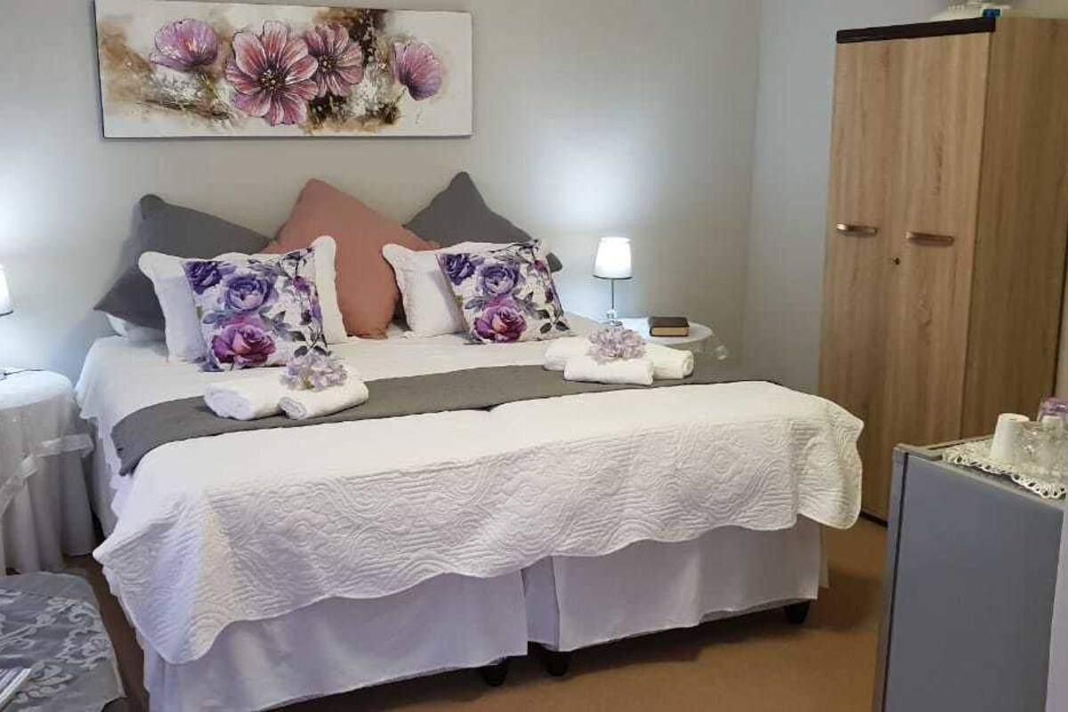 Un dormitorio ordenado con una cama, dos mesitas de noche, un armario y un cuadro en la pared.