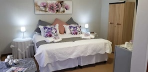 Une chambre à coucher bien rangée, avec un lit, deux tables de chevet, une commode, une armoire et un tableau accroché au mur.