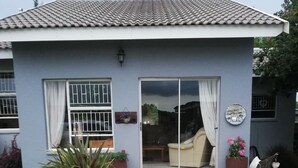 Una casa con techo de tejas, puerta corrediza de vidrio, un patio con un banco y plantas en macetas.