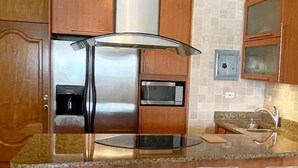 A kitchen with wooden cabinets, a stainless steel refrigerator, a microwave, and a glass-top island with chairs.