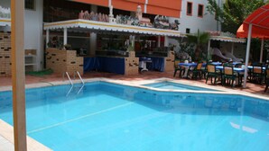 Una piscina con bar y zona de estar, rodeada por un edificio con paredes exteriores naranja y blanco.