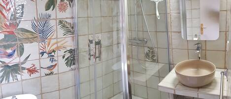Un baño con cabina de ducha de vidrio, un lavabo blanco y un espejo encima.