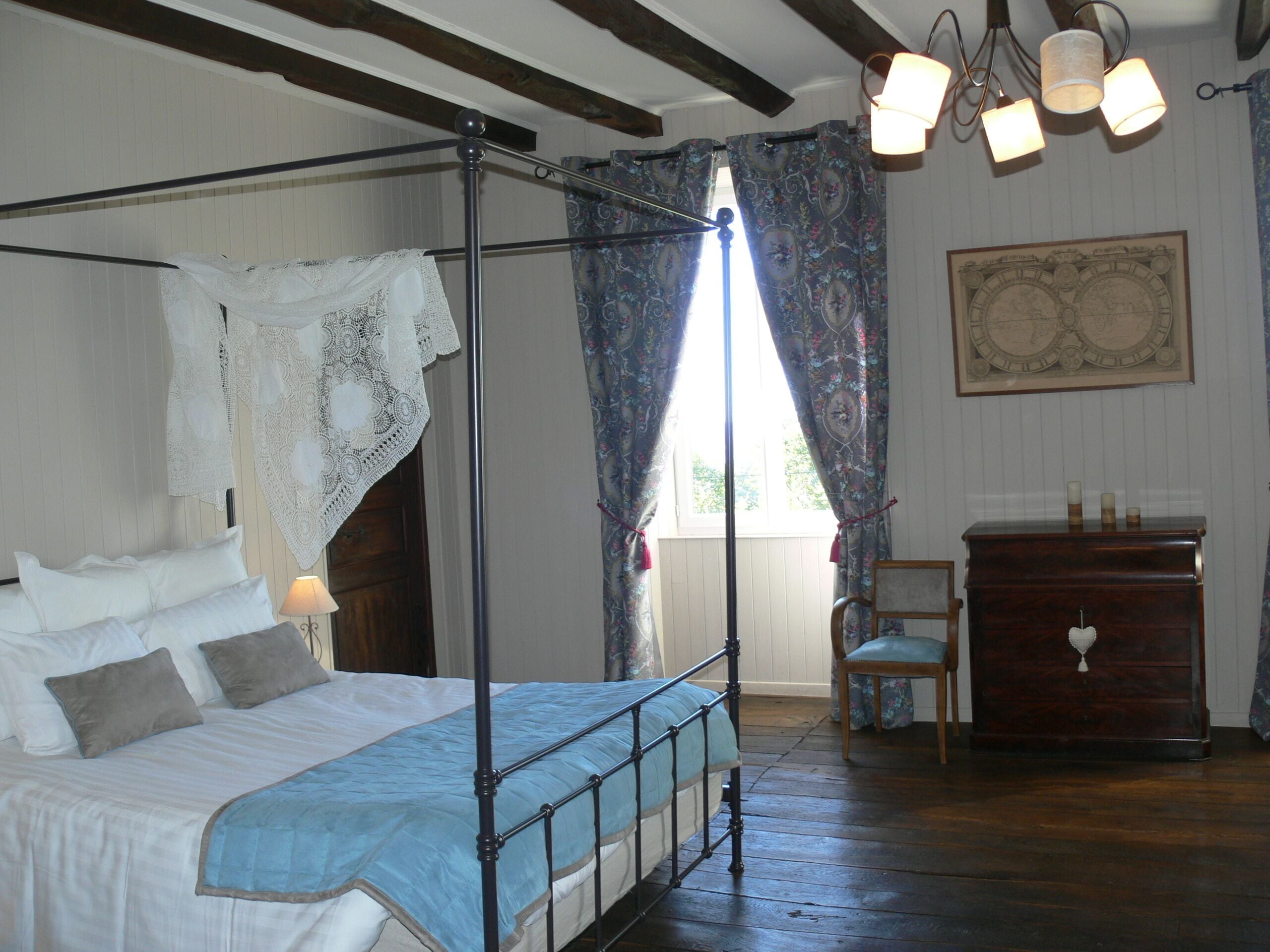 Una cama con dosel de madera y encaje, un aparador de madera y una silla en una habitación con suelo de madera y techo inclinado.