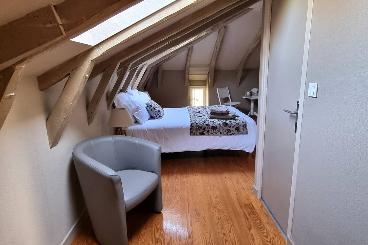 Ein schmaler, schräg zulaufender Raum mit einem Bett, einem Sessel und Holzboden.
