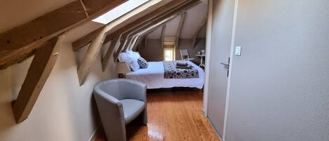 A narrow, sloped room with a bed, a chair, and a wooden floor.