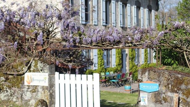 Un edificio rústico con cerca blanca y enredaderas moradas floreciendo. Se observan letreros que indican 'Château de la Bouteille' y 'CleVacances'.
