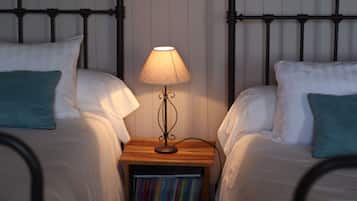Une chambre avec deux lits, chacun agrémenté de draps blancs et d’oreillers turquoise. Une table de chevet avec une lampe et une bibliothèque se trouve entre les deux lits.