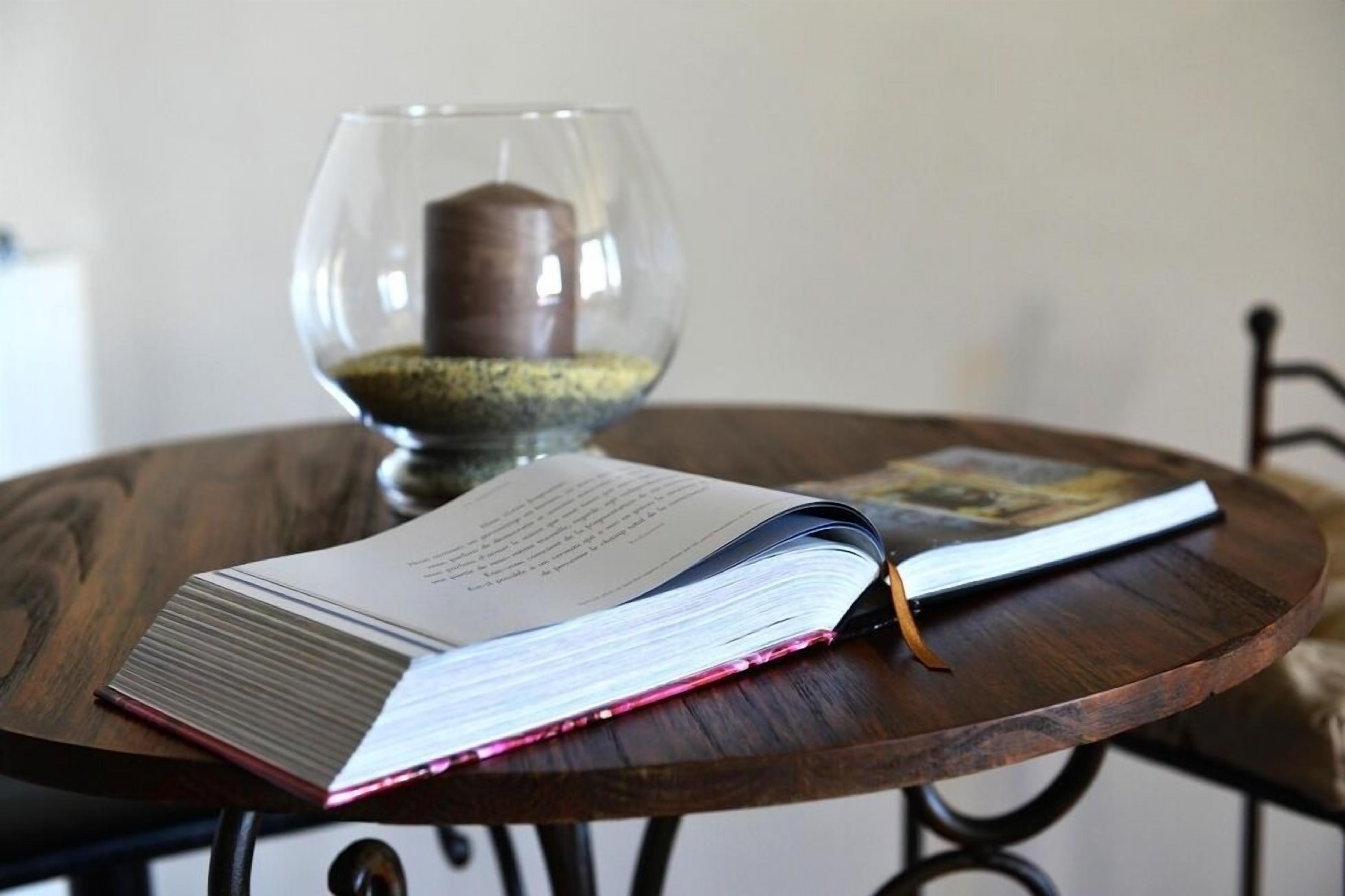Un libro abierto sobre una mesa de madera, con un vaso de agua y una vela al fondo.