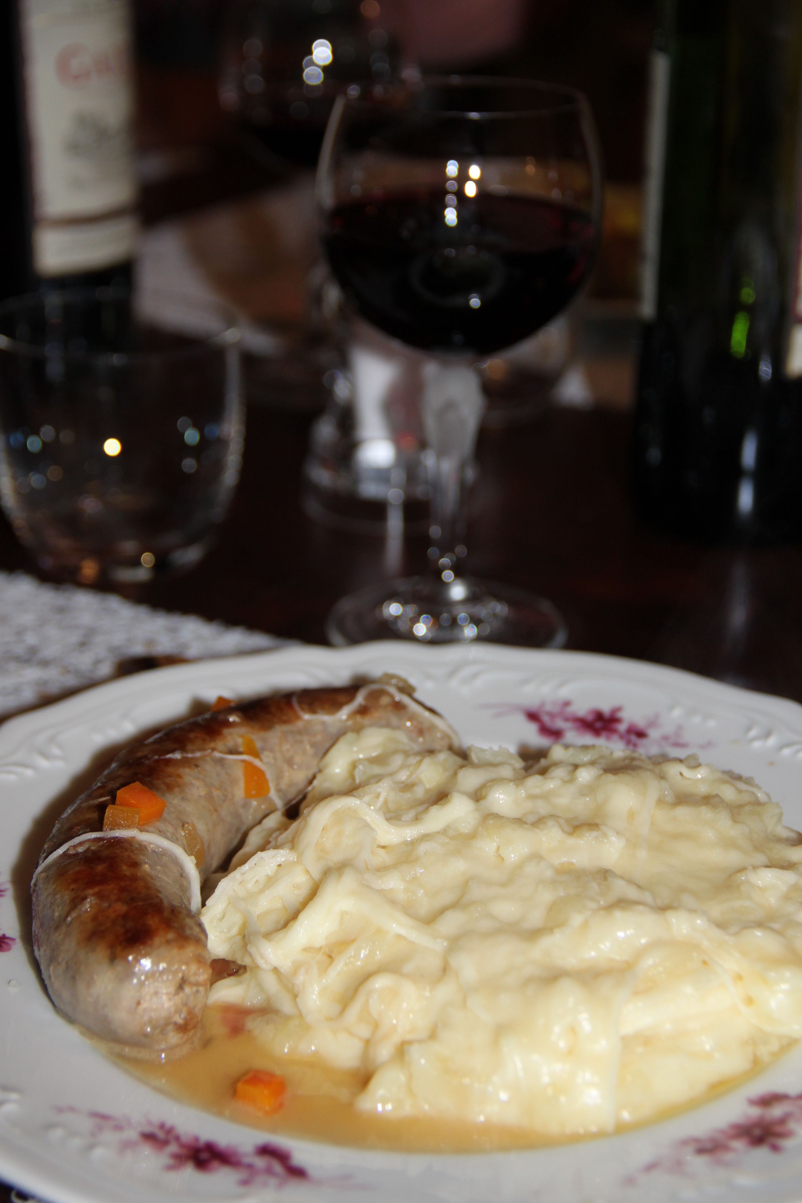 Ein Teller mit Wurst und Kartoffelpüree, dazu ein Glas Rotwein.