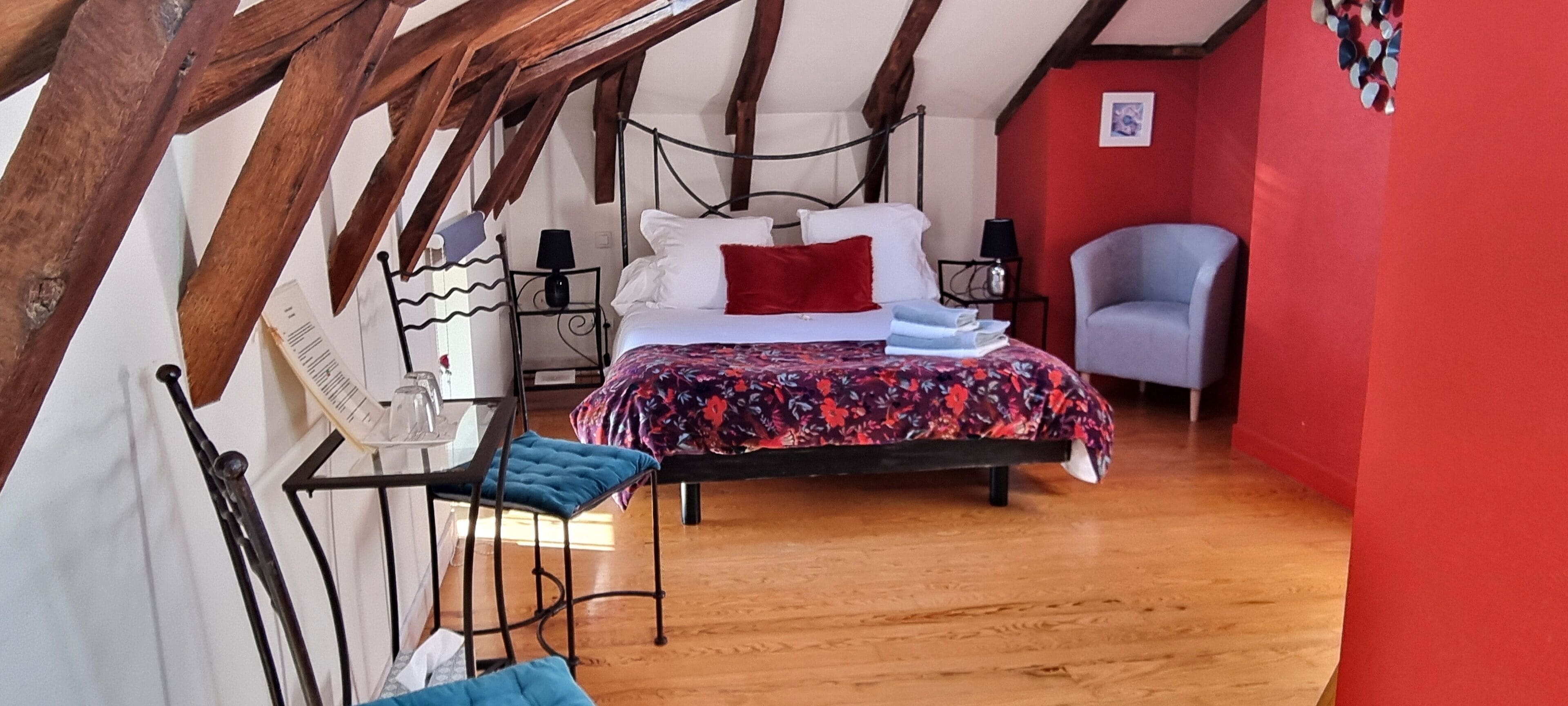 Een slaapkamer met een bed, een stoel, een bureau en een rode muur.