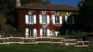 Un edificio de dos pisos con base de pared de piedra, contraventanas blancas y techo de tejas.