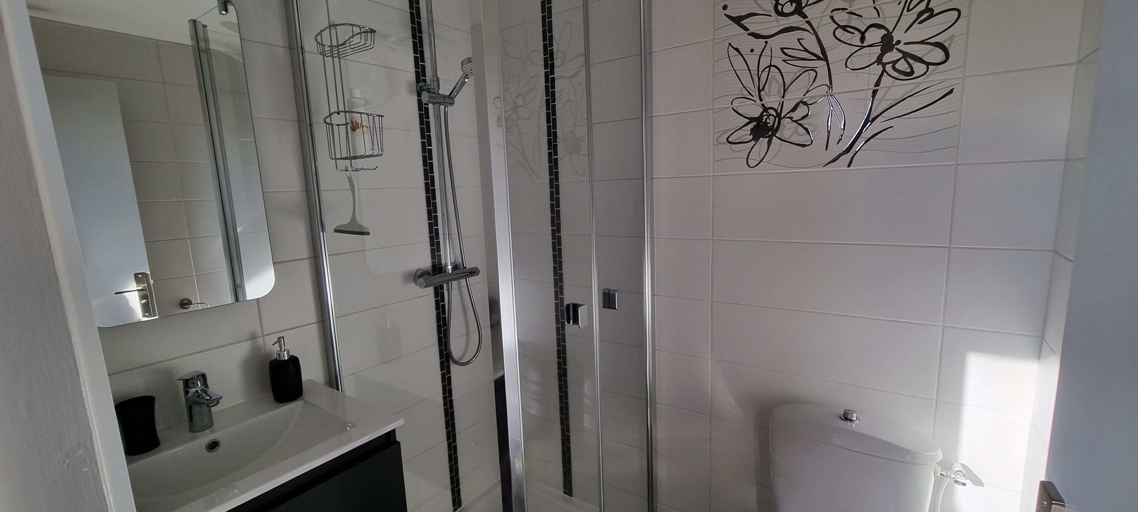 Un baño moderno con cabina de ducha de vidrio, un espejo grande y un inodoro.