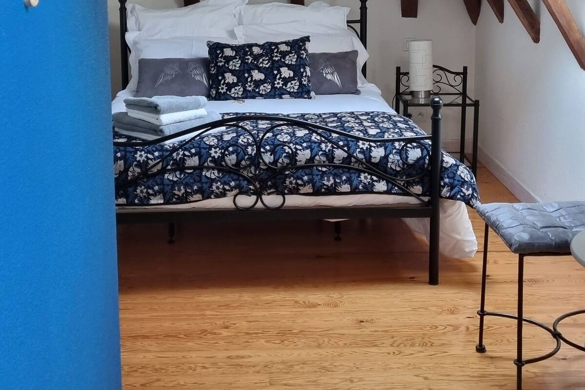 Ein Schlafzimmer mit Holzbalkendecke, einem Bett mit floralem Bettbezug, einem Nachttisch und einem Stuhl.