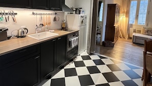 A modern kitchen with black cabinets, a black and white checkered floor, and a wooden ceiling beam.