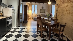 A kitchen with a black and white checkered floor, wooden beams on the ceiling, a dining table with chairs, and a stone wall.