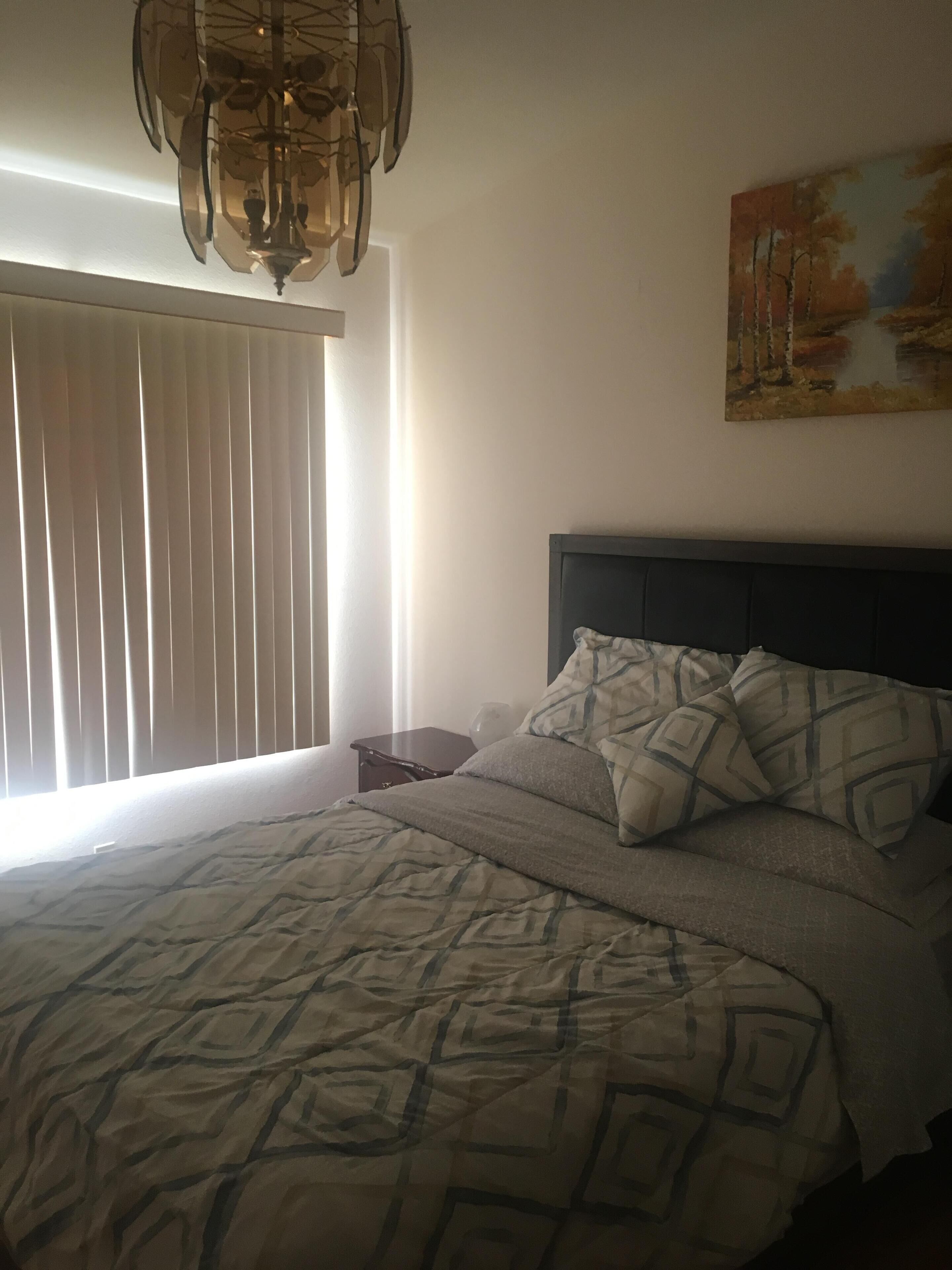 Um quarto com cama, mesa de cabeceira, um quadro e uma janela com persianas.