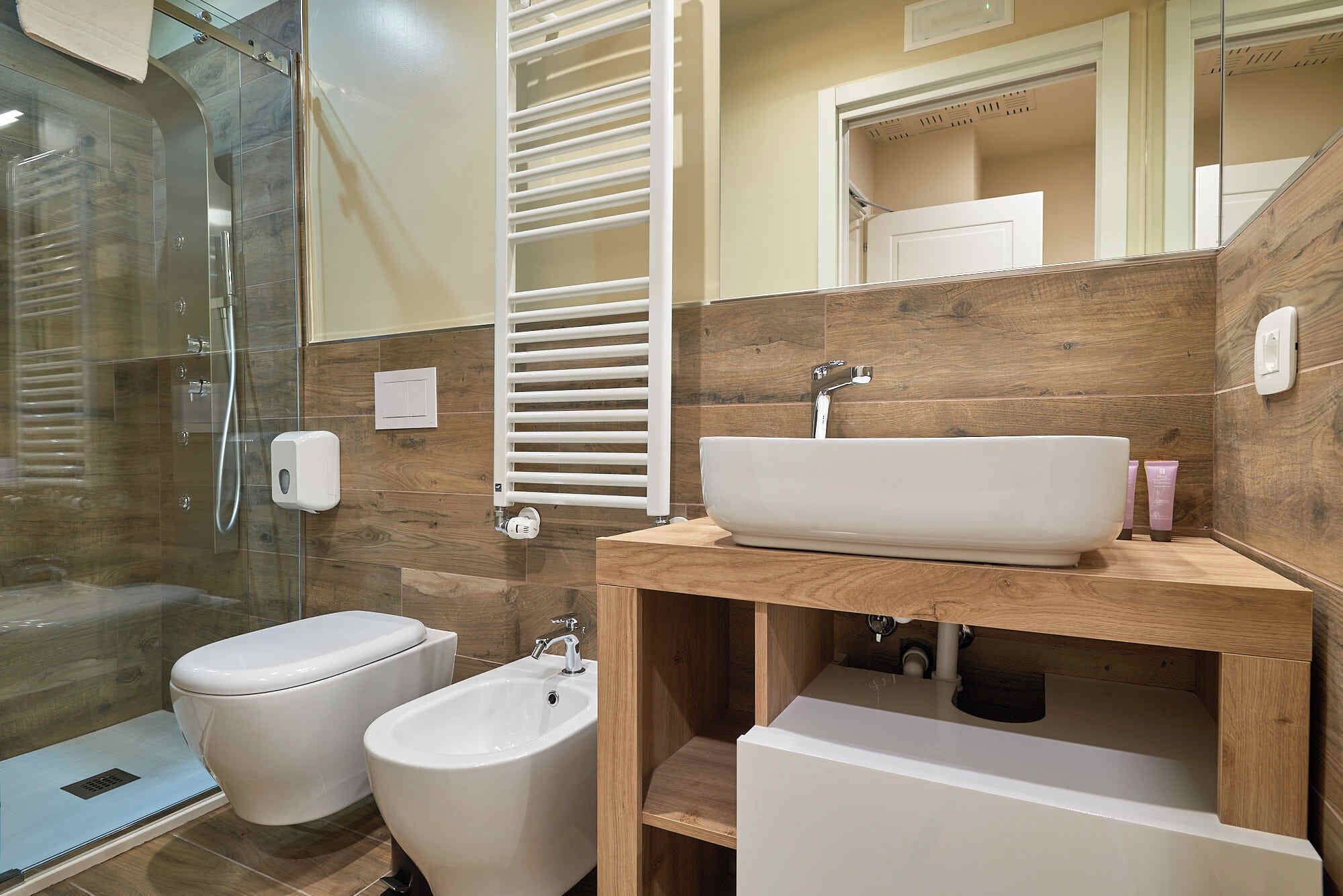 Un baño moderno con cabina de ducha de vidrio, un bidé, un lavabo con tocador de madera y un espejo sobre el lavabo.