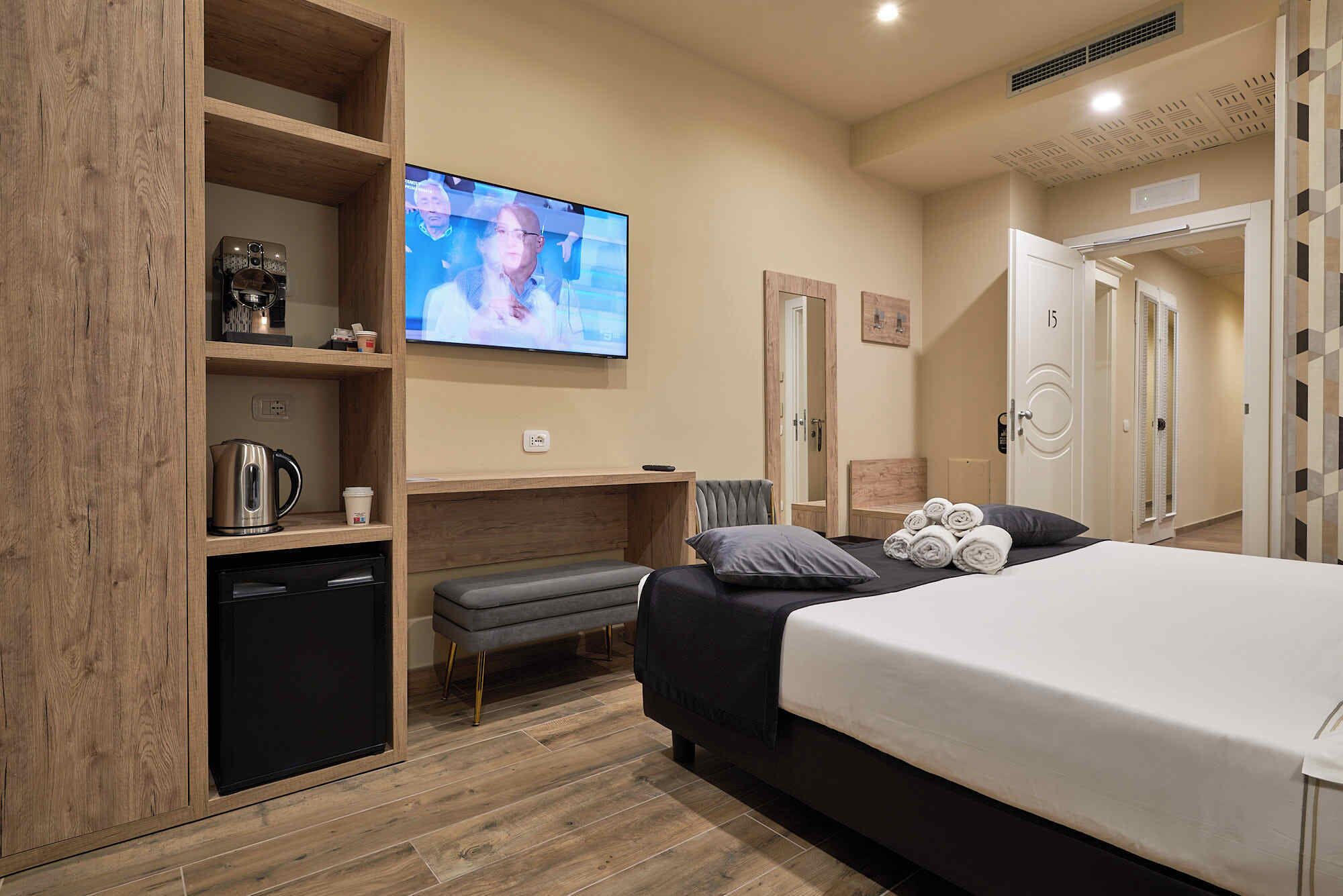 A hotel room with a bed, a TV, a kitchenette, and a bathroom.