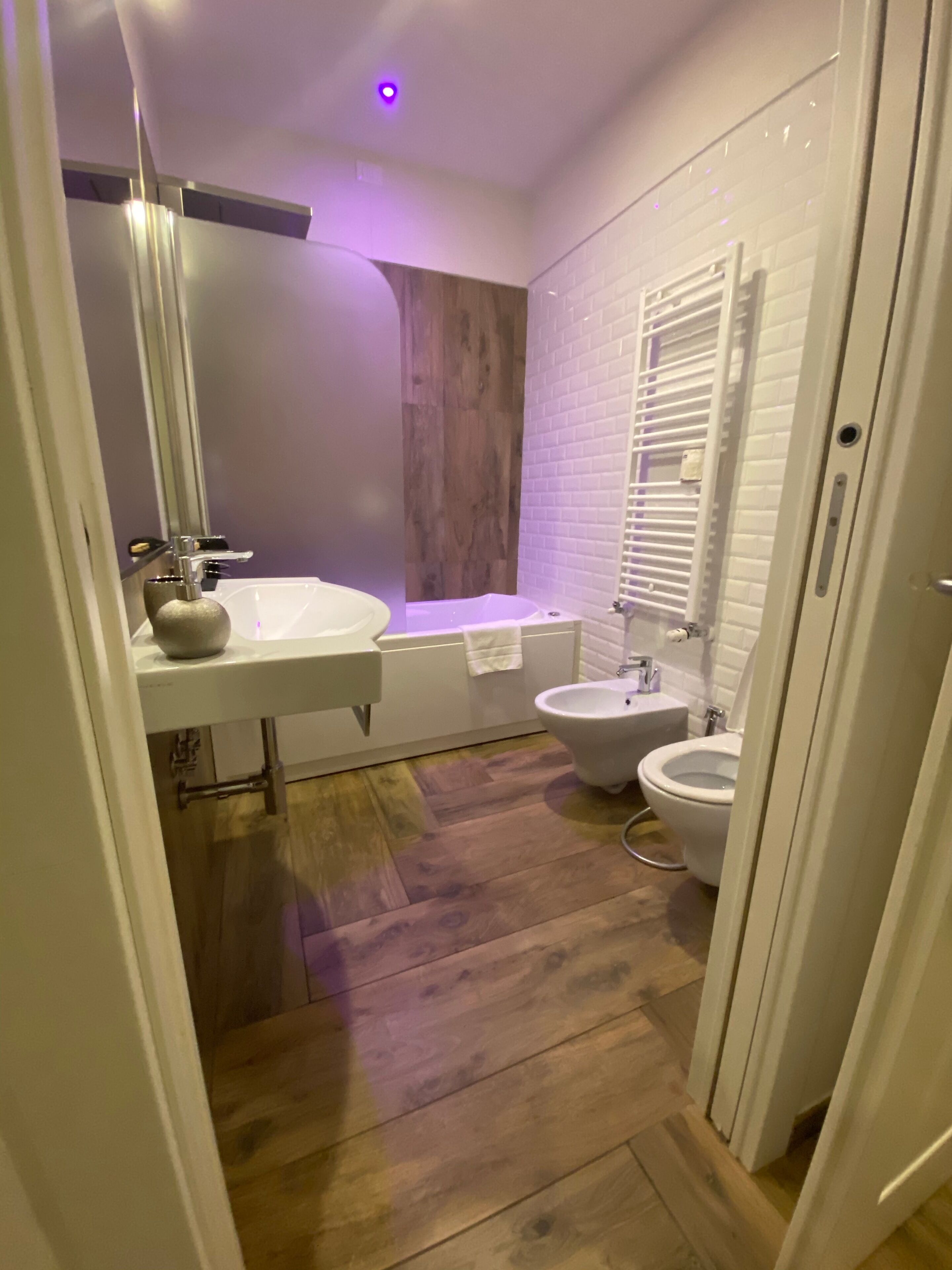 A bathroom with a white sink, a bathtub, a bidet, and a wooden floor.