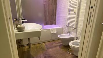 A bathroom with a white sink, a bathtub, a bidet, and a wooden floor.
