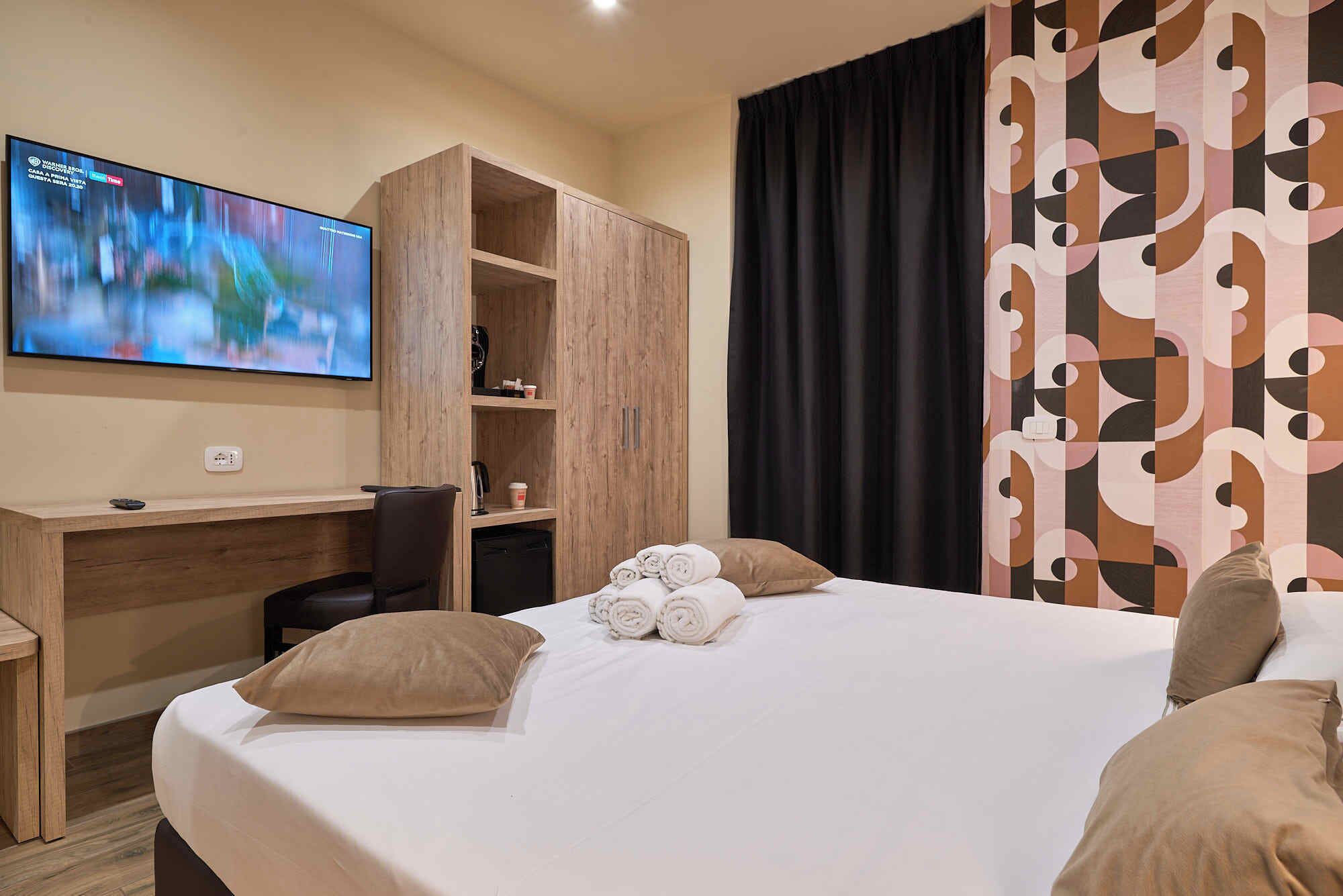 Hotellihuone, jossa on sänky, työpöytä, televisio ja vaatekaappi.
