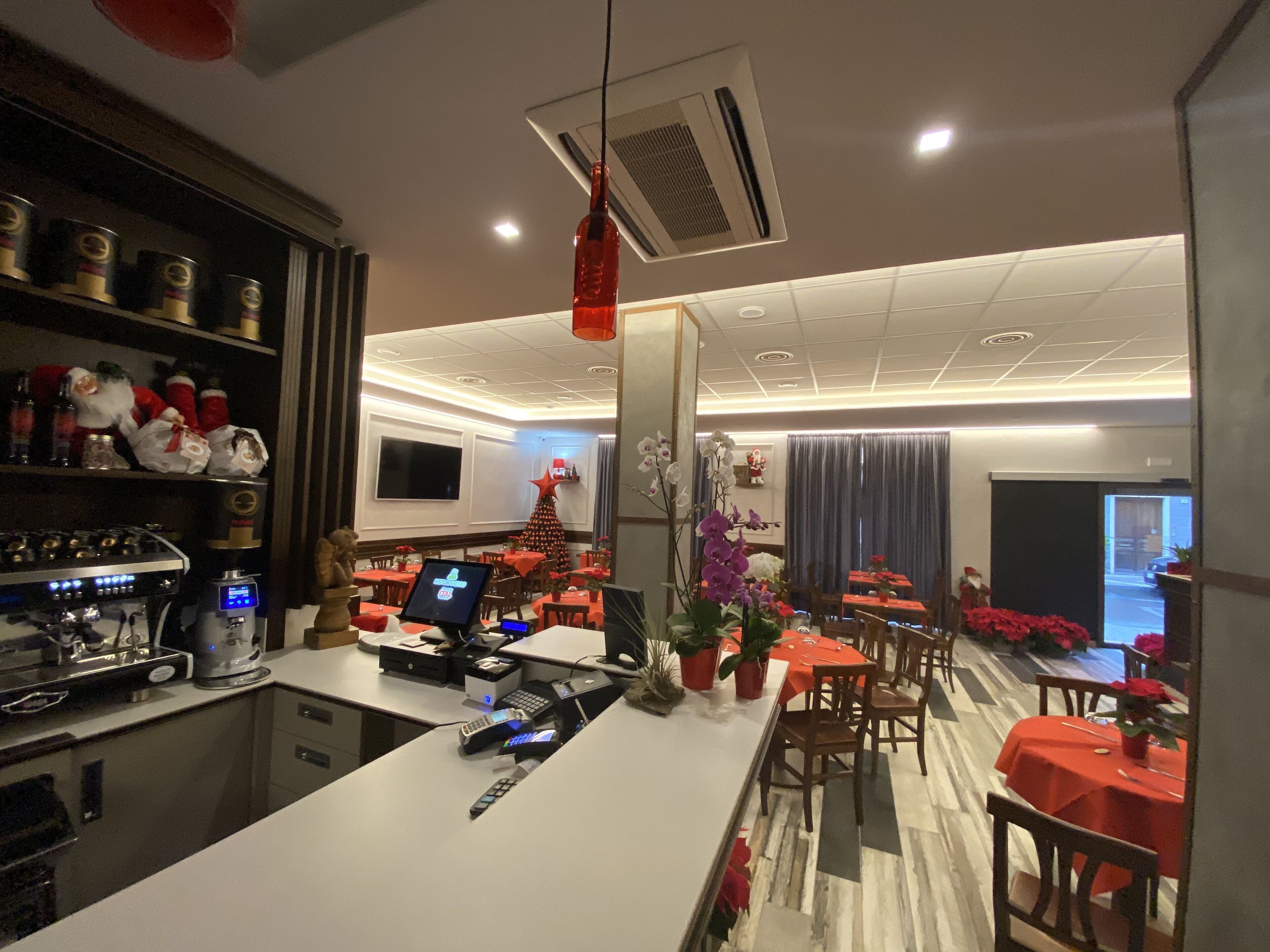 Un restaurante con área de bar, mesas con manteles rojos y un árbol de Navidad.