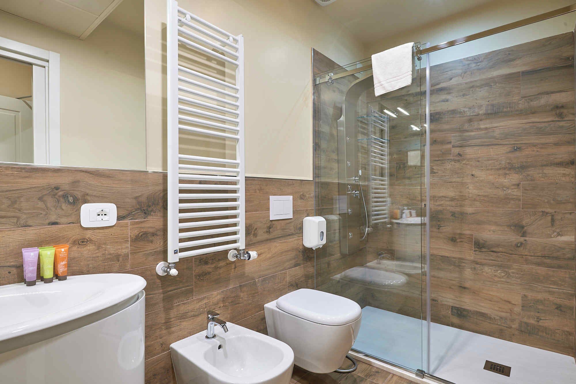 A modern bathroom with a glass shower enclosure, a white toilet, a bidet, and a vanity with a mirror.