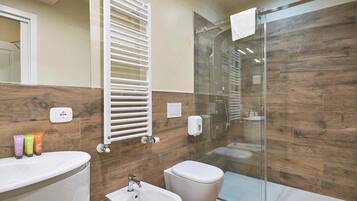 A modern bathroom with a glass shower enclosure, a white toilet, a bidet, and a vanity with a mirror.