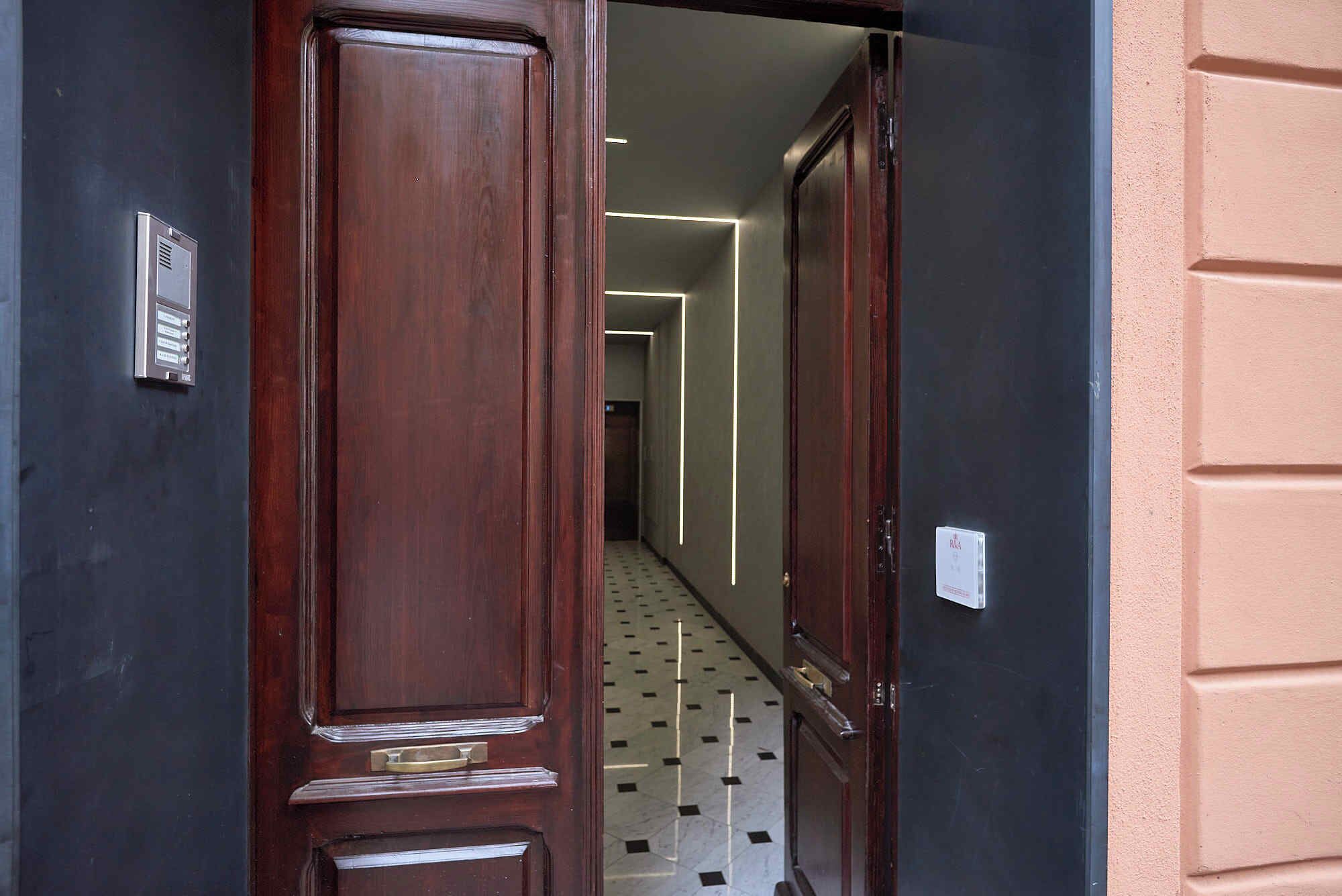 A hallway with a wooden door, a metal intercom, and a patterned floor.