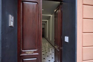 A hallway with a wooden door, a metal intercom, and a patterned floor.