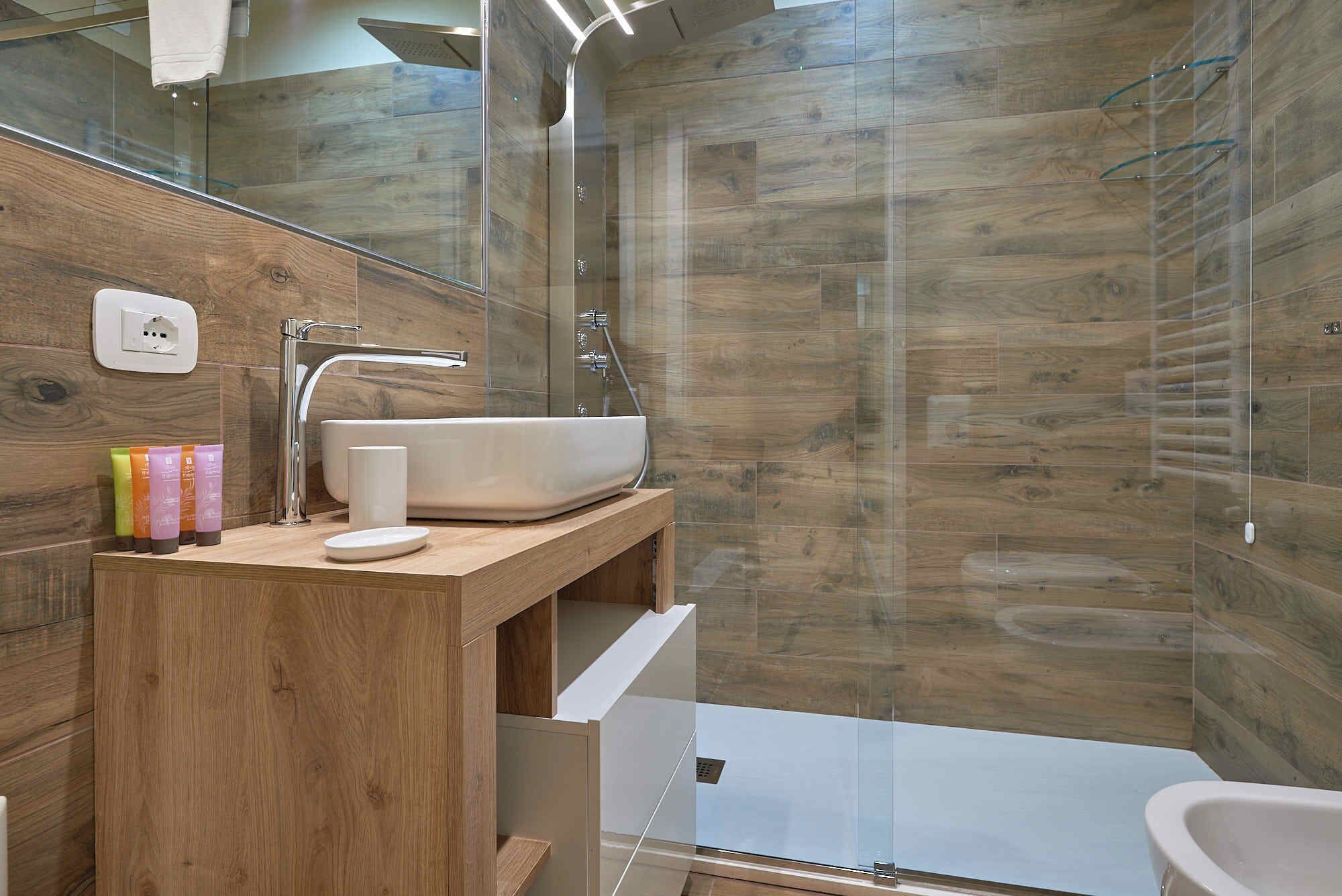A modern bathroom with a wooden vanity, a large sink, and a glass shower enclosure.