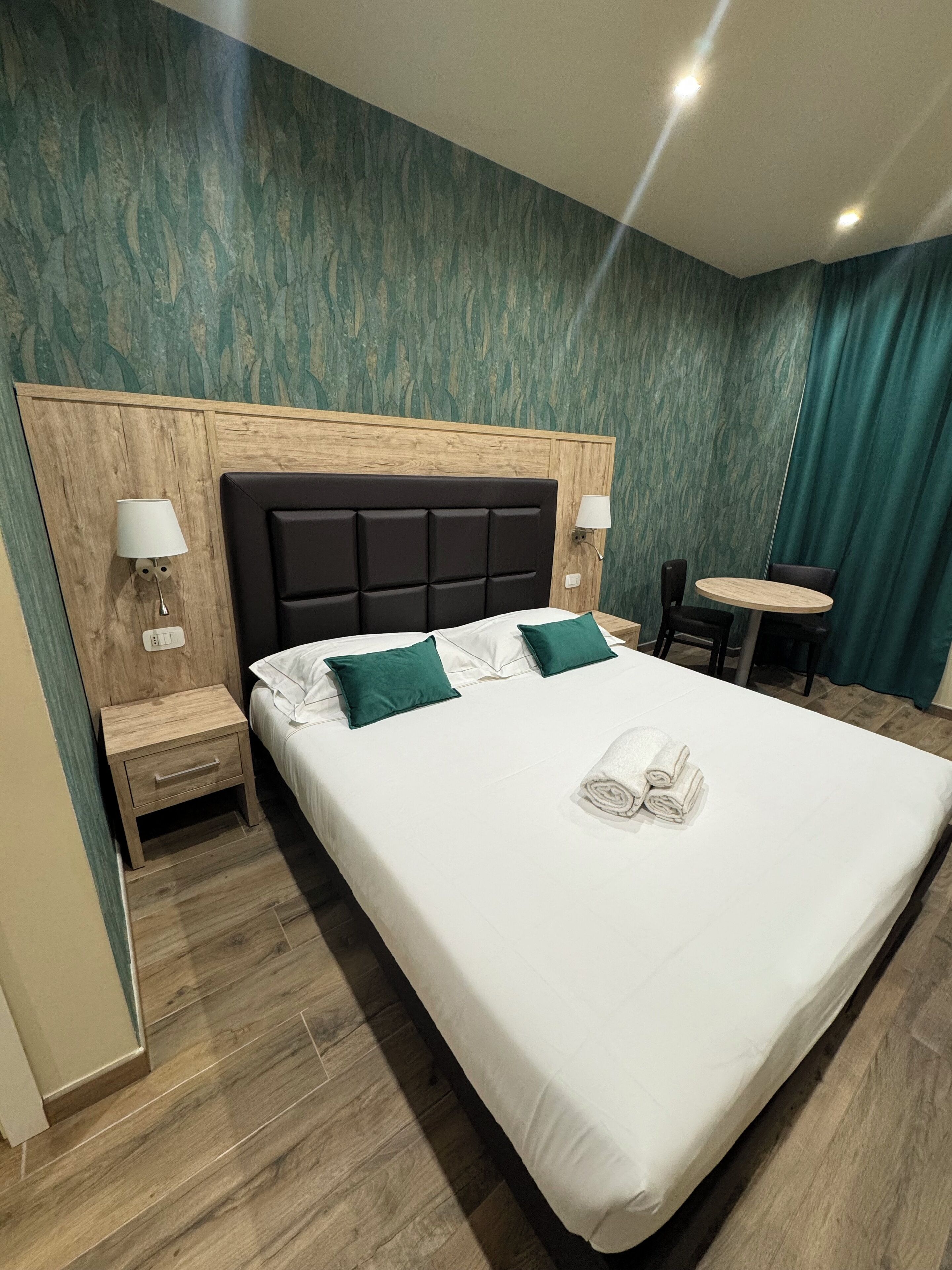 A hotel room with a large bed, two bedside tables, a small round table, and a chair.
